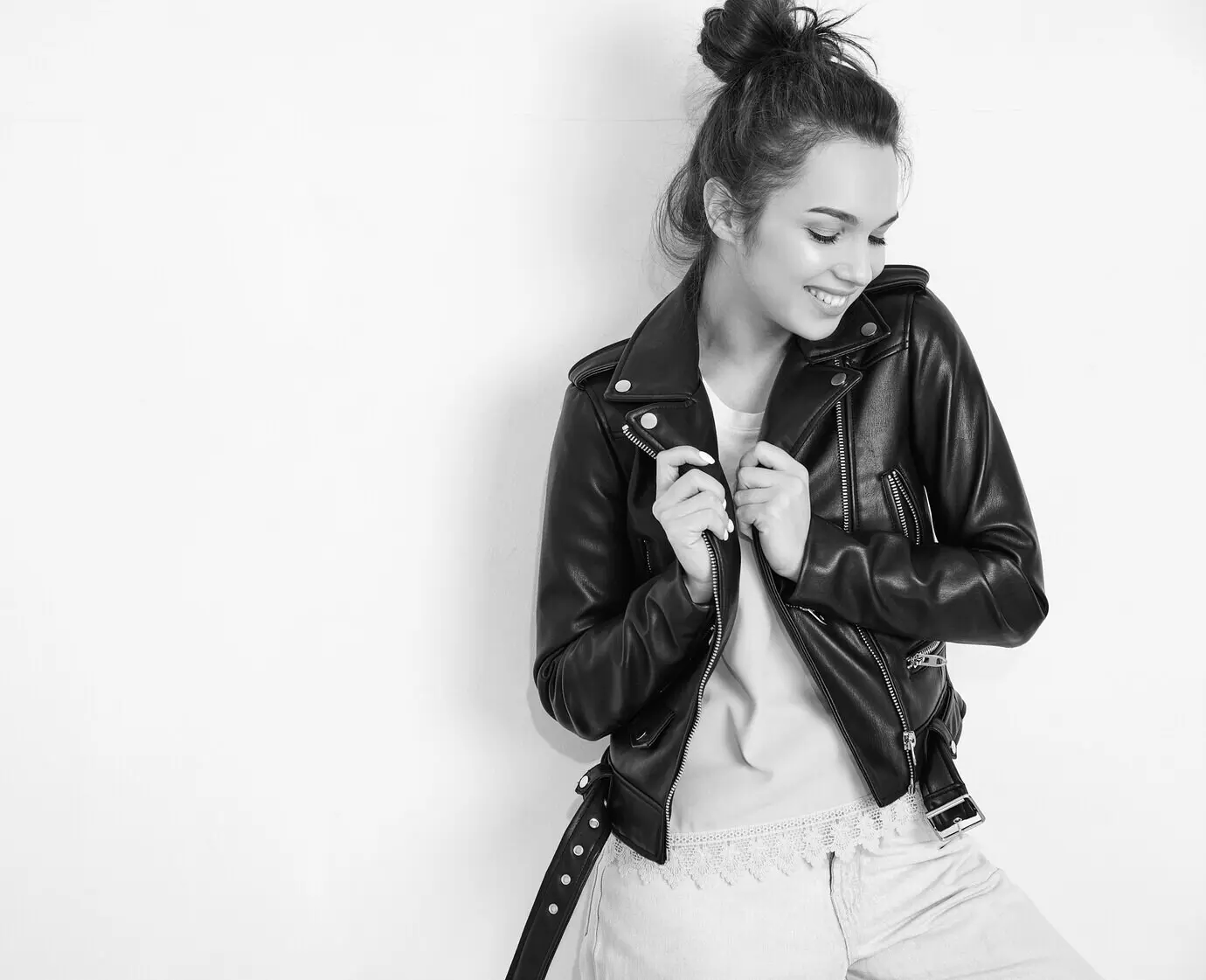 Porträt eines jungen, schönen, brünetten weiblichen Models mit Nude-Make-up, das eine sommerliche Hipster-Biker-Lederjacke trägt und nahe einer Wand posiert.